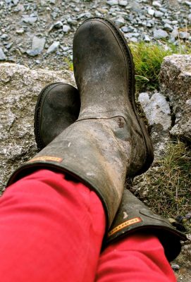 a person sitting crossed legged with red trousers and welly boots., which need a wellington Boot Rack to hang them on