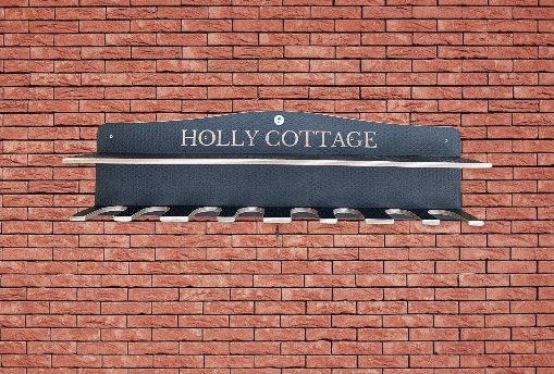 Wooden Brown welly Rack personalised with Holly Cottage on a red brick wall.